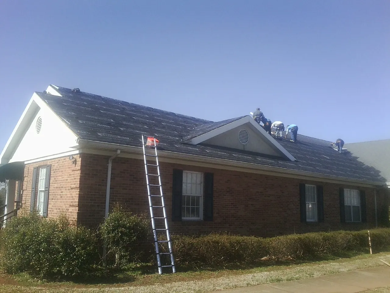 Crew tearing shingles off a brick ranch roof with a ladder set — Metal Roof Repair work by our crew in Sonora
