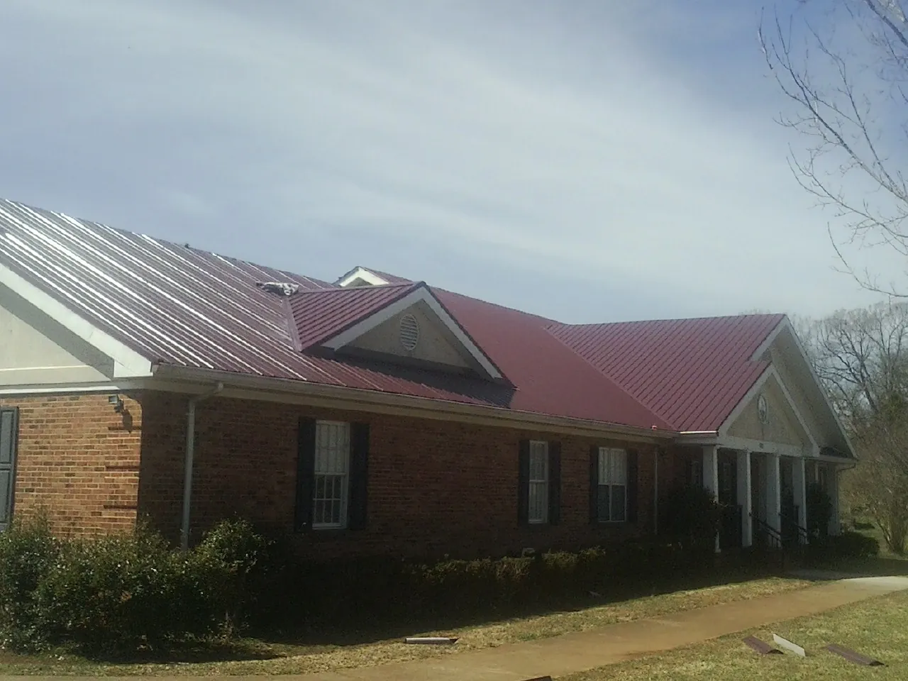 Red metal roof with gabled entries on a long brick building, from a Hail Damage Roof Repair job in Sonora