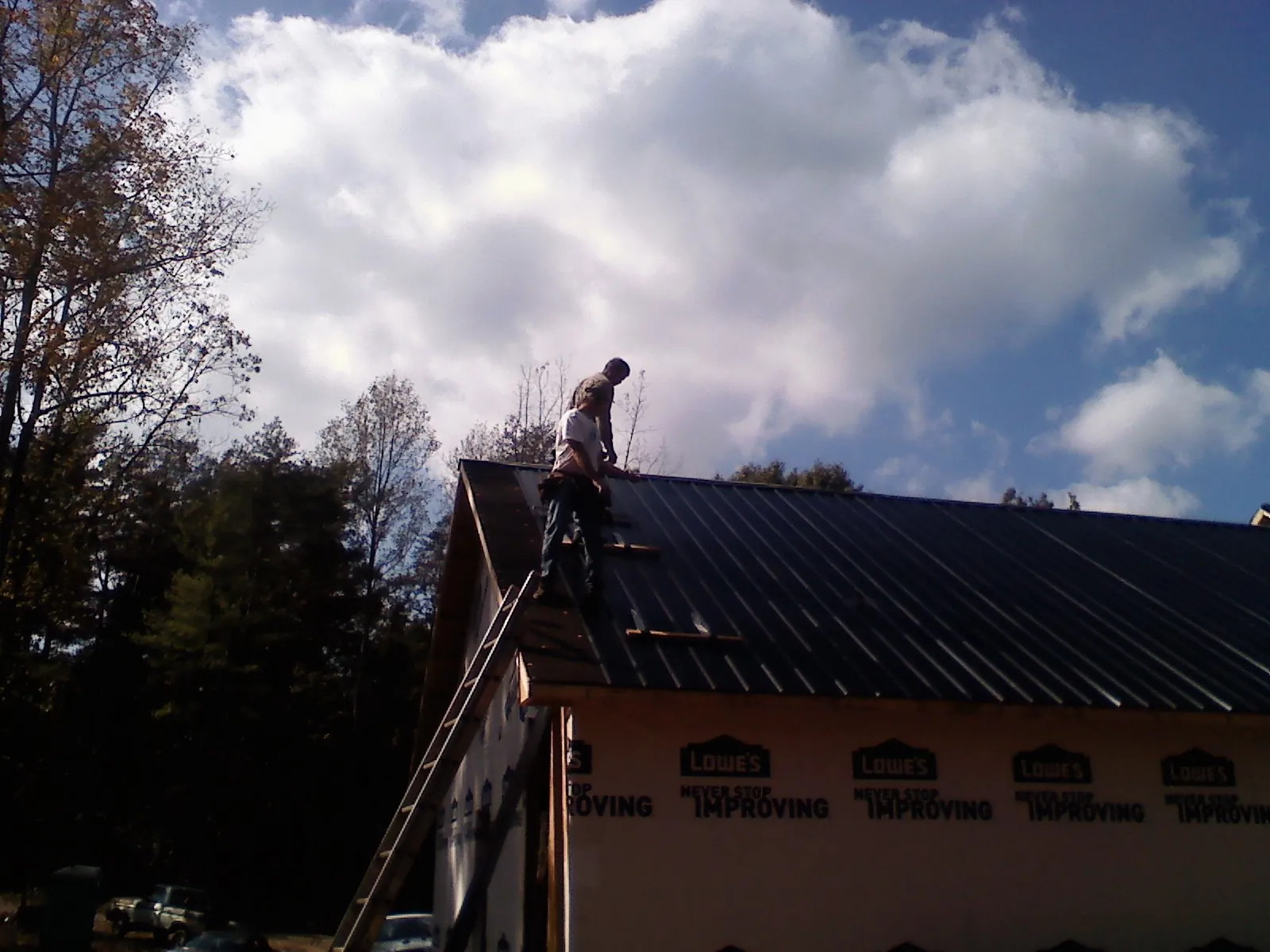Roofer fastening dark metal panels high against a cloudy sky, from a Roof Inspection job in Sonora