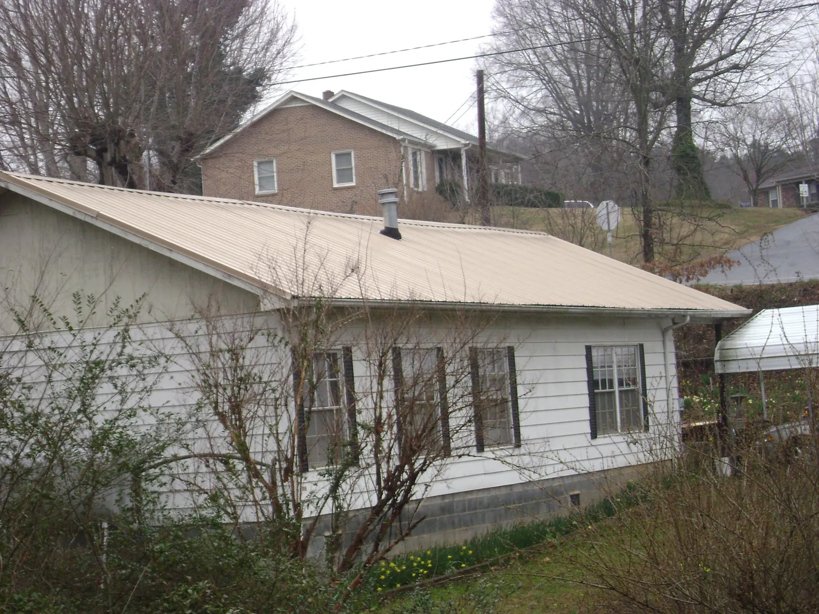 Tan metal roof on a white sided house set into a hillside — Commercial Roofing by Roofing Brothers in Sonora